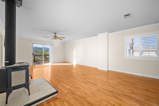 living room with crown molding, ceiling fan, light hardwood / wood-style floors, and a wood stove