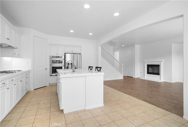 kitchen featuring white cabinetry, appliances with stainless steel finishes, a kitchen island with sink, and light tile patterned flooring