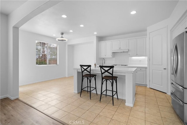 kitchen featuring white cabinetry, an island with sink, a breakfast bar area, stovetop, and stainless steel refrigerator