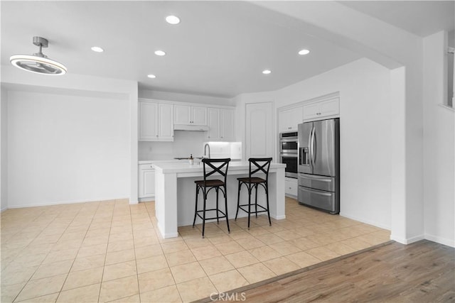 kitchen with white cabinets, stainless steel appliances, a breakfast bar, light tile patterned floors, and a center island with sink