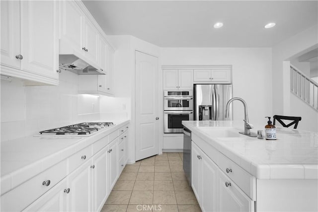 kitchen featuring stainless steel appliances, tile counters, light tile patterned flooring, white cabinets, and sink