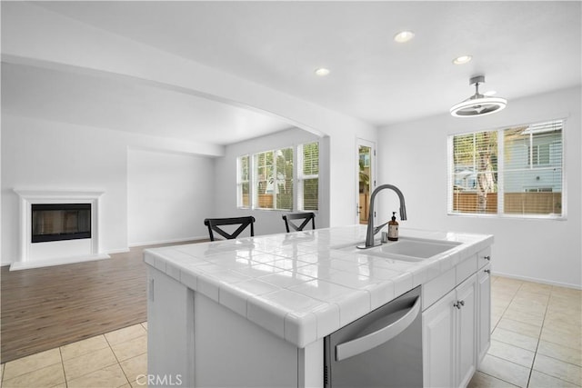 kitchen with white cabinetry, a center island with sink, tile counters, light tile patterned flooring, and dishwasher