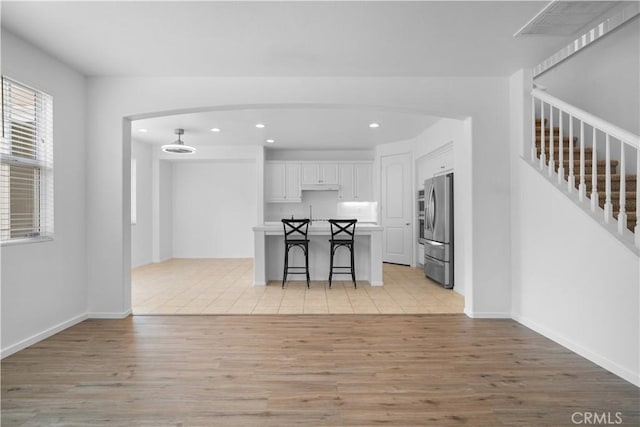 kitchen with light wood-type flooring, white cabinets, a breakfast bar, and stainless steel fridge