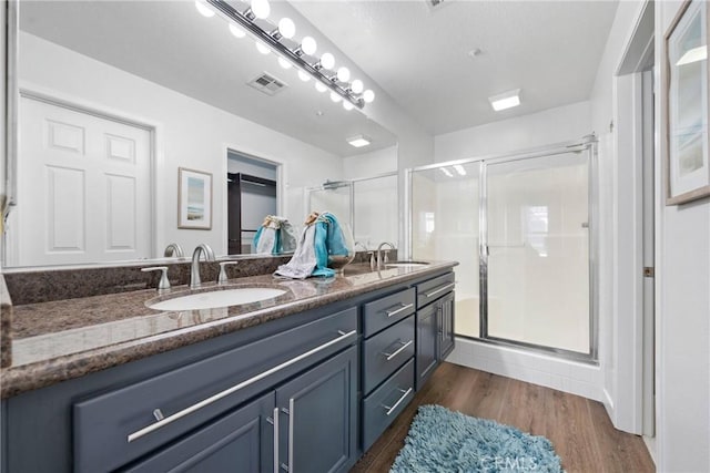 full bath featuring wood finished floors, a sink, visible vents, and a shower stall