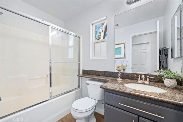 full bathroom featuring hardwood / wood-style flooring, vanity, shower / bath combination with glass door, and toilet