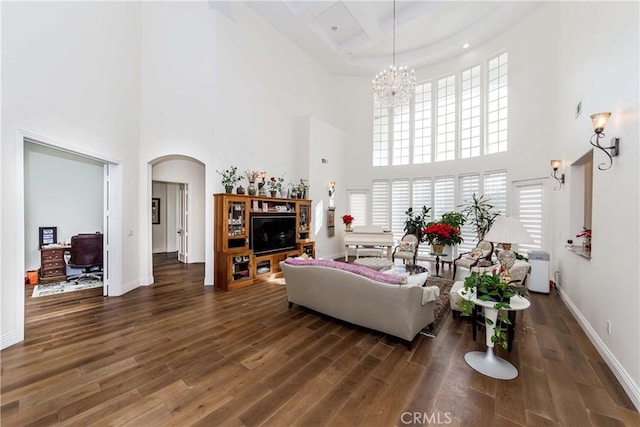 living room featuring dark wood-type flooring, a chandelier, and a towering ceiling