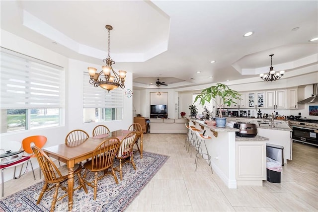 dining area featuring sink, ceiling fan with notable chandelier, and a tray ceiling