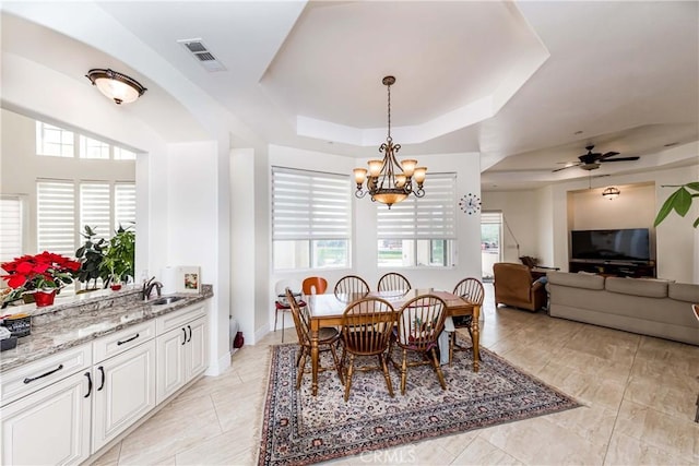 dining area featuring plenty of natural light, ceiling fan with notable chandelier, a raised ceiling, and sink