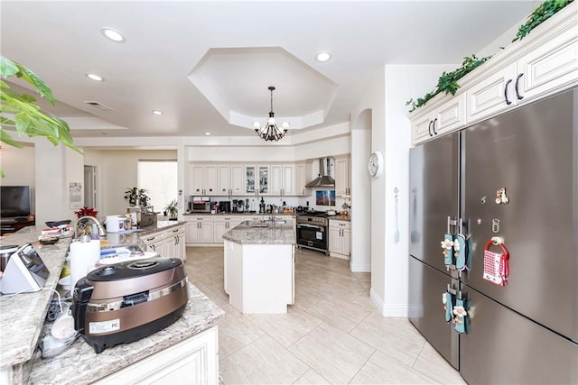 kitchen featuring white cabinetry, stainless steel appliances, a raised ceiling, a kitchen island with sink, and sink