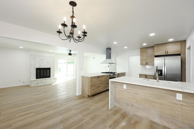 kitchen with island range hood, stainless steel appliances, hanging light fixtures, a high end fireplace, and ceiling fan with notable chandelier