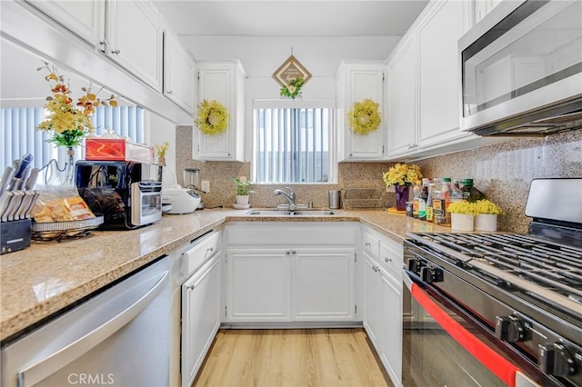 kitchen featuring sink, white cabinets, backsplash, stainless steel appliances, and light stone countertops