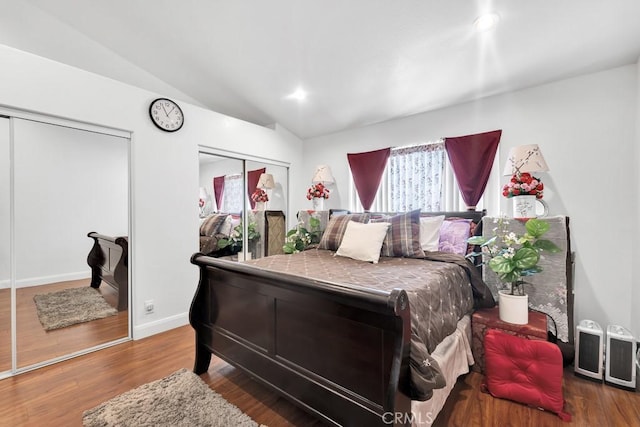 bedroom featuring multiple closets, vaulted ceiling, baseboards, and wood finished floors