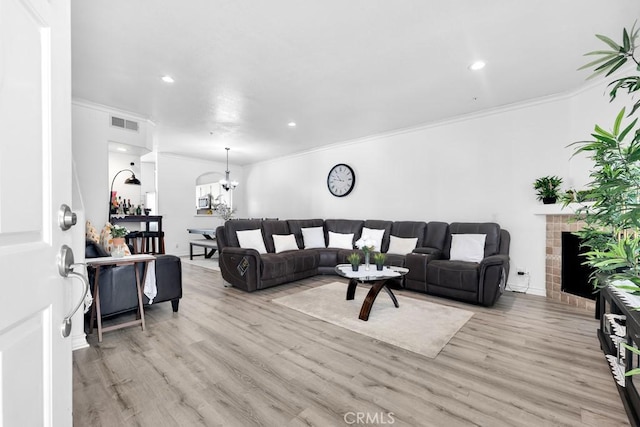 living room featuring light wood-style floors, a tile fireplace, visible vents, and crown molding