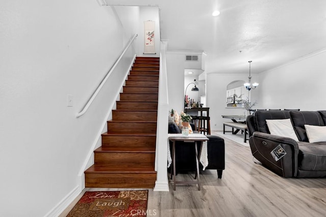 stairway featuring a chandelier, wood finished floors, visible vents, baseboards, and crown molding