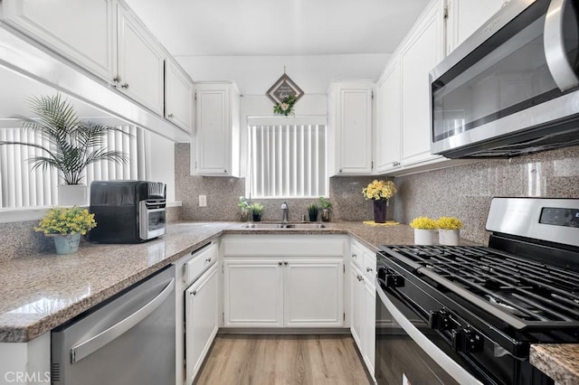 kitchen with appliances with stainless steel finishes, light wood-style floors, white cabinetry, and a sink