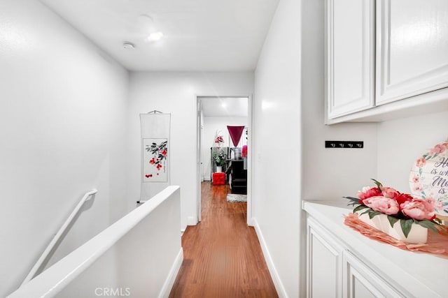 hallway with light wood-style flooring, an upstairs landing, and baseboards