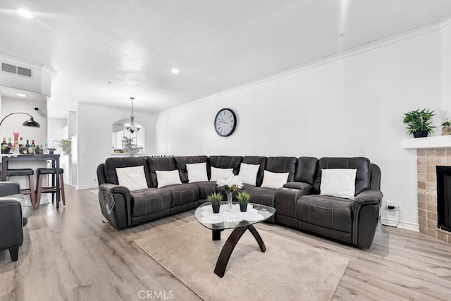 living area featuring light wood-style flooring, a fireplace, visible vents, baseboards, and crown molding