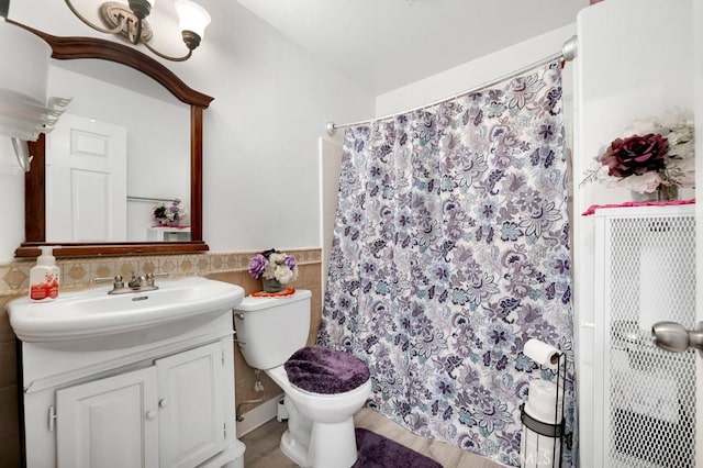 bathroom featuring toilet, a wainscoted wall, a shower with curtain, vanity, and tile walls