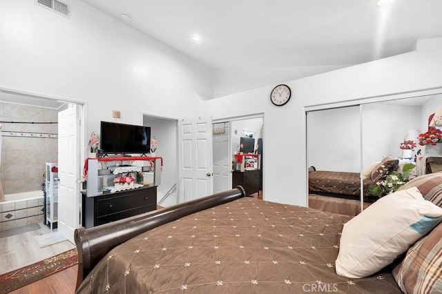 bedroom featuring visible vents, wood finished floors, ensuite bathroom, high vaulted ceiling, and two closets