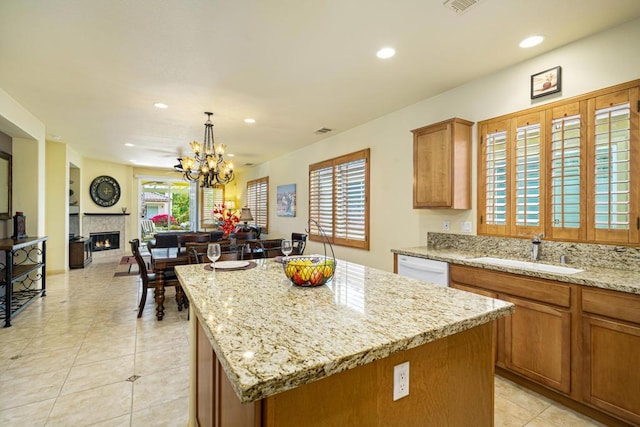 kitchen with decorative light fixtures, a kitchen island, sink, light stone countertops, and a chandelier