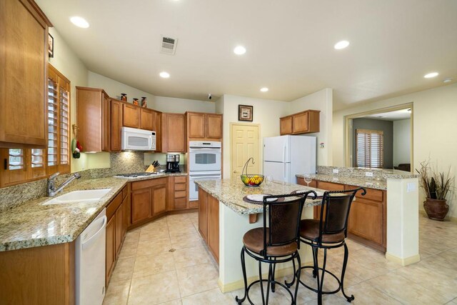 kitchen featuring a kitchen island, a kitchen bar, sink, white appliances, and light stone countertops