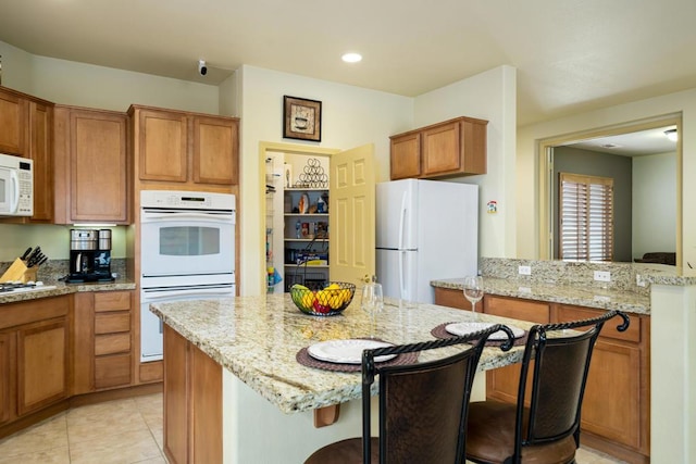 kitchen with light stone counters, a breakfast bar, white appliances, and light tile patterned flooring