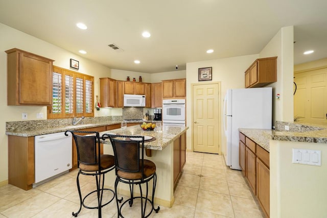 kitchen featuring a breakfast bar area, white appliances, light tile patterned flooring, light stone countertops, and a center island