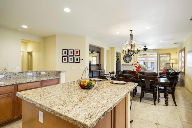 kitchen featuring a kitchen island, hanging light fixtures, light stone countertops, light tile patterned floors, and ceiling fan with notable chandelier