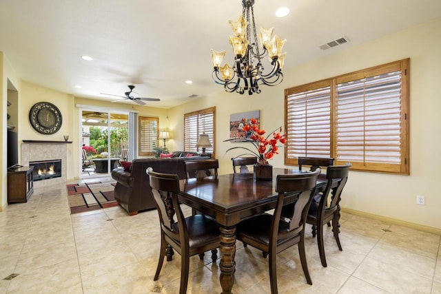 dining area featuring ceiling fan with notable chandelier, light tile patterned floors, and a tiled fireplace