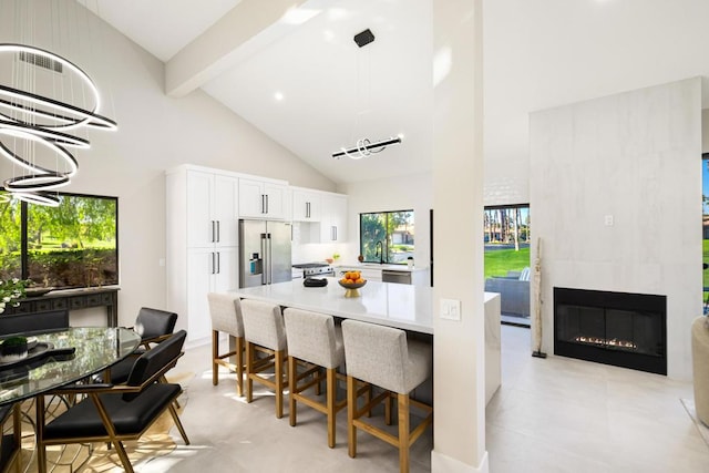 kitchen with high vaulted ceiling, a tile fireplace, beamed ceiling, stainless steel appliances, and white cabinets