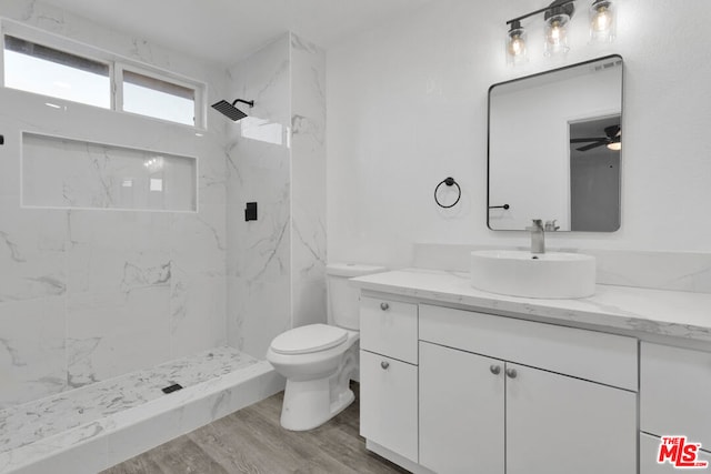 bathroom featuring toilet, vanity, ceiling fan, hardwood / wood-style flooring, and a tile shower