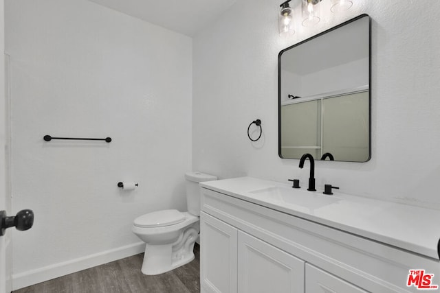 bathroom with hardwood / wood-style floors, toilet, a shower with door, and vanity