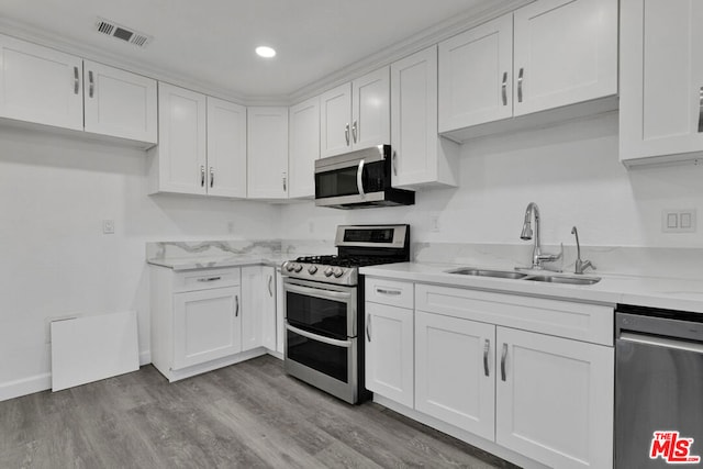 kitchen with white cabinetry, stainless steel appliances, light hardwood / wood-style floors, sink, and light stone counters