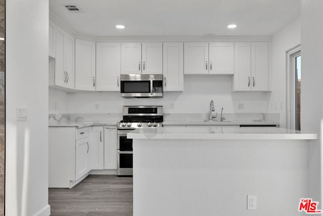 kitchen featuring light hardwood / wood-style floors, kitchen peninsula, appliances with stainless steel finishes, white cabinets, and sink