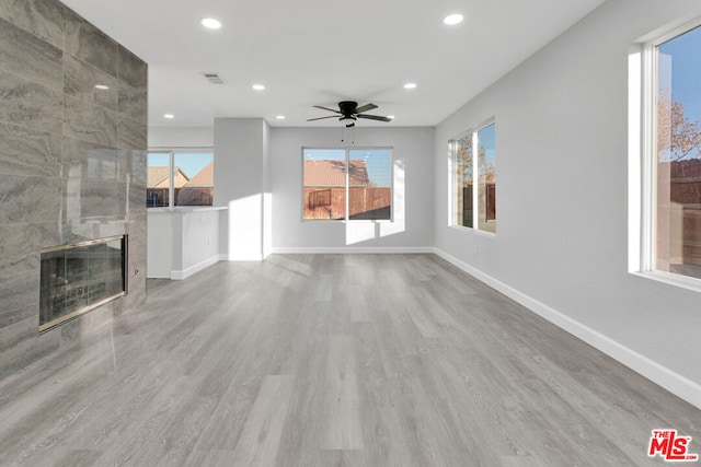 unfurnished living room with ceiling fan, light hardwood / wood-style floors, and a tiled fireplace