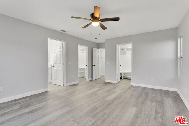 unfurnished bedroom with ensuite bathroom, light hardwood / wood-style floors, ceiling fan, a closet, and a walk in closet