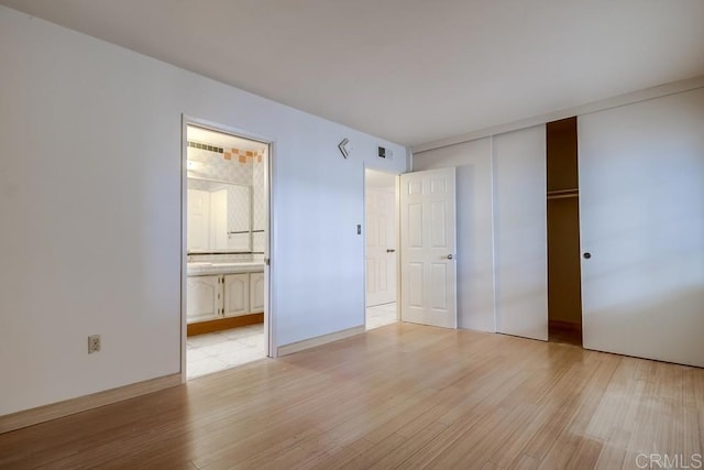 unfurnished bedroom with ensuite bath, a closet, and light hardwood / wood-style flooring