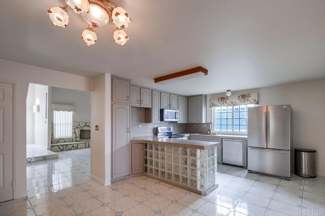 kitchen with tasteful backsplash, kitchen peninsula, gray cabinets, and stainless steel appliances