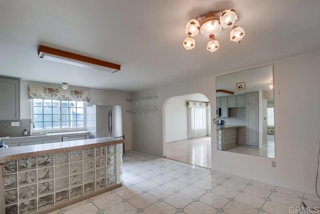 kitchen featuring a notable chandelier, decorative backsplash, stainless steel refrigerator, and sink