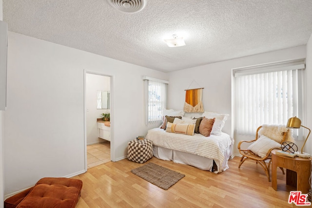 bedroom with connected bathroom, light hardwood / wood-style flooring, and a textured ceiling