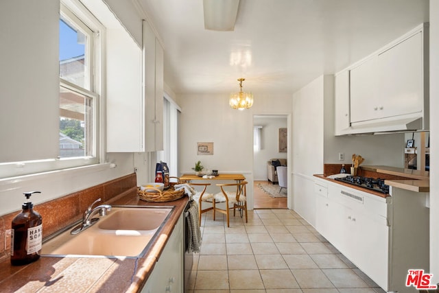 kitchen with a notable chandelier, pendant lighting, sink, white cabinetry, and stainless steel gas cooktop