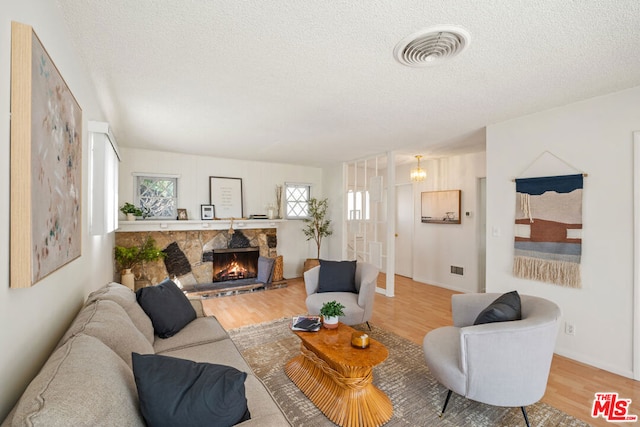 living room with a stone fireplace, a textured ceiling, and hardwood / wood-style flooring