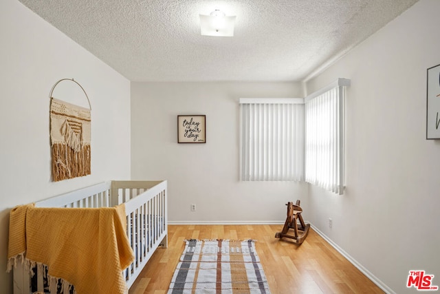 bedroom with wood-type flooring, a crib, and a textured ceiling