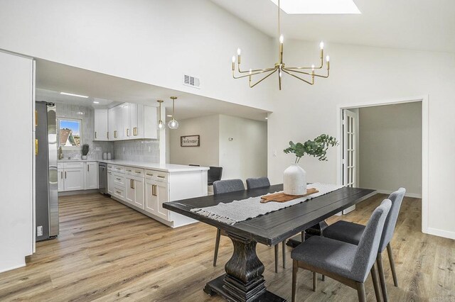 dining area with a skylight, light hardwood / wood-style floors, high vaulted ceiling, and a notable chandelier