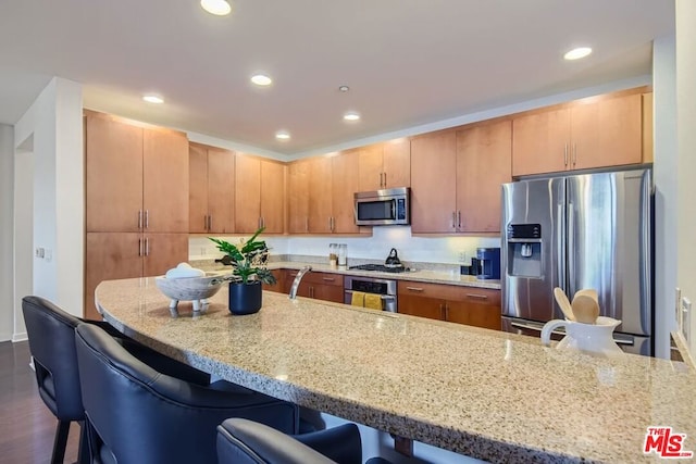 kitchen with light stone countertops, a breakfast bar, appliances with stainless steel finishes, and dark hardwood / wood-style floors