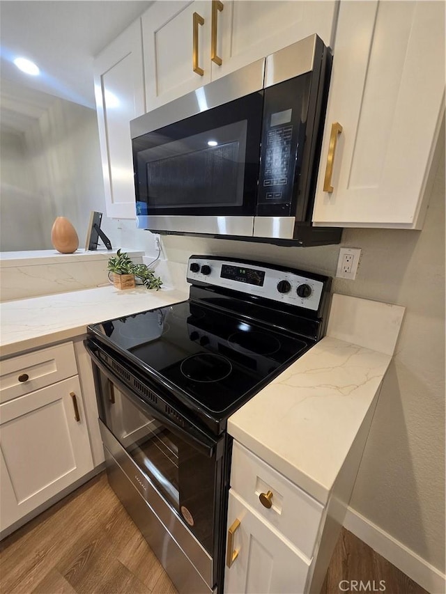 kitchen with light wood-type flooring, light stone countertops, stainless steel appliances, and white cabinetry