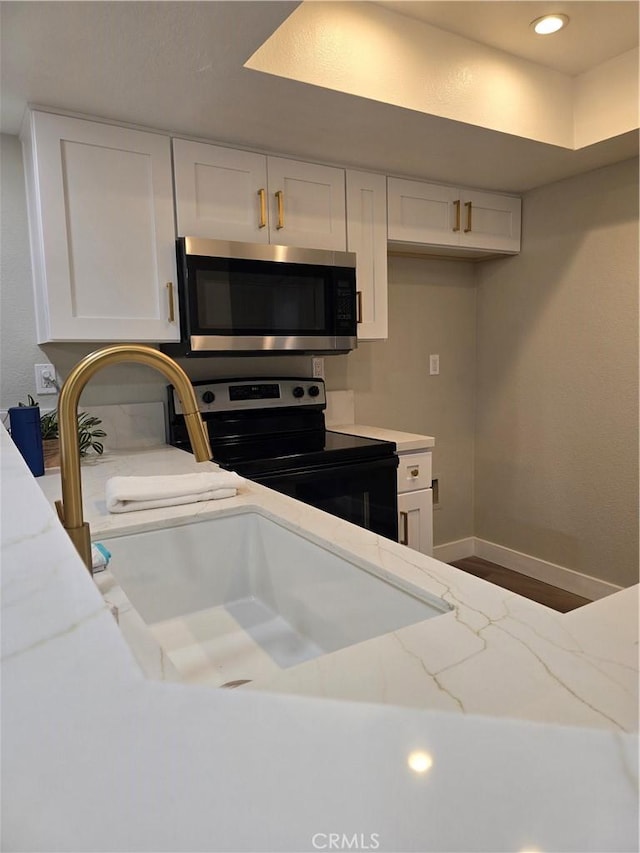 kitchen featuring light stone countertops, white cabinets, black range with electric stovetop, and sink