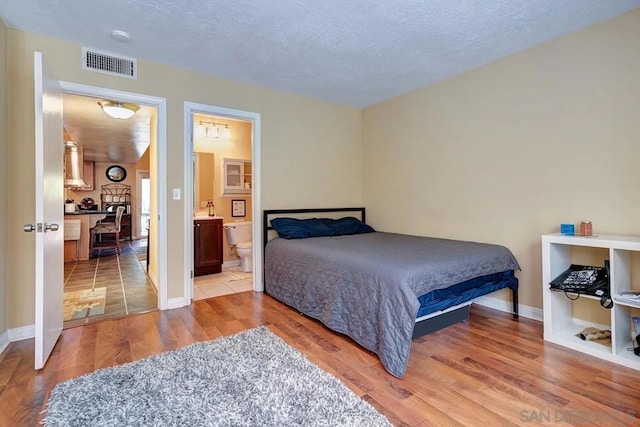 bedroom featuring ensuite bathroom, a textured ceiling, and hardwood / wood-style floors