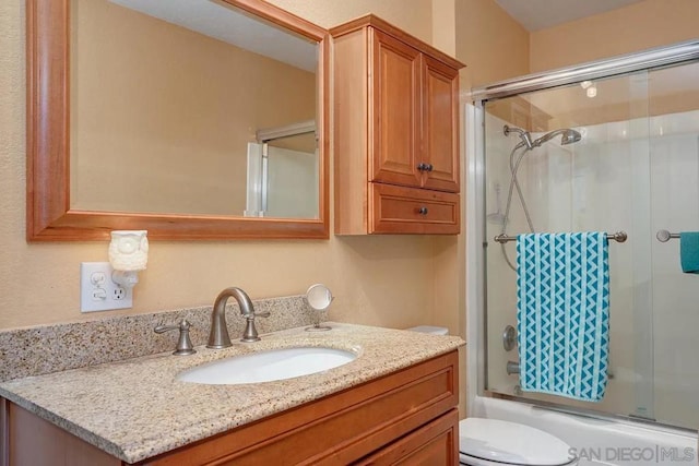 full bathroom featuring combined bath / shower with glass door, vanity, and toilet