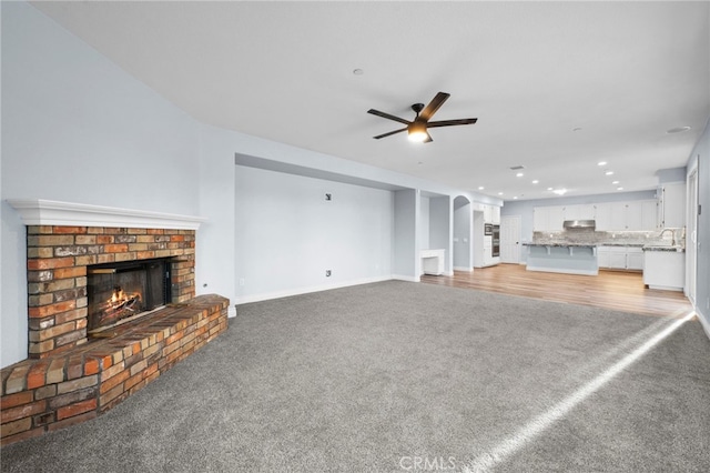 unfurnished living room featuring light carpet, ceiling fan, a fireplace, and sink